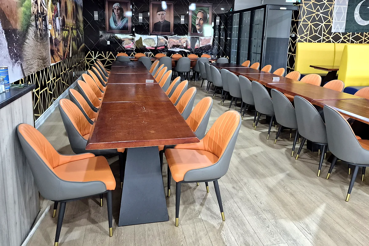 Dining room with long wooden tables, orange and grey chairs and a mural wall