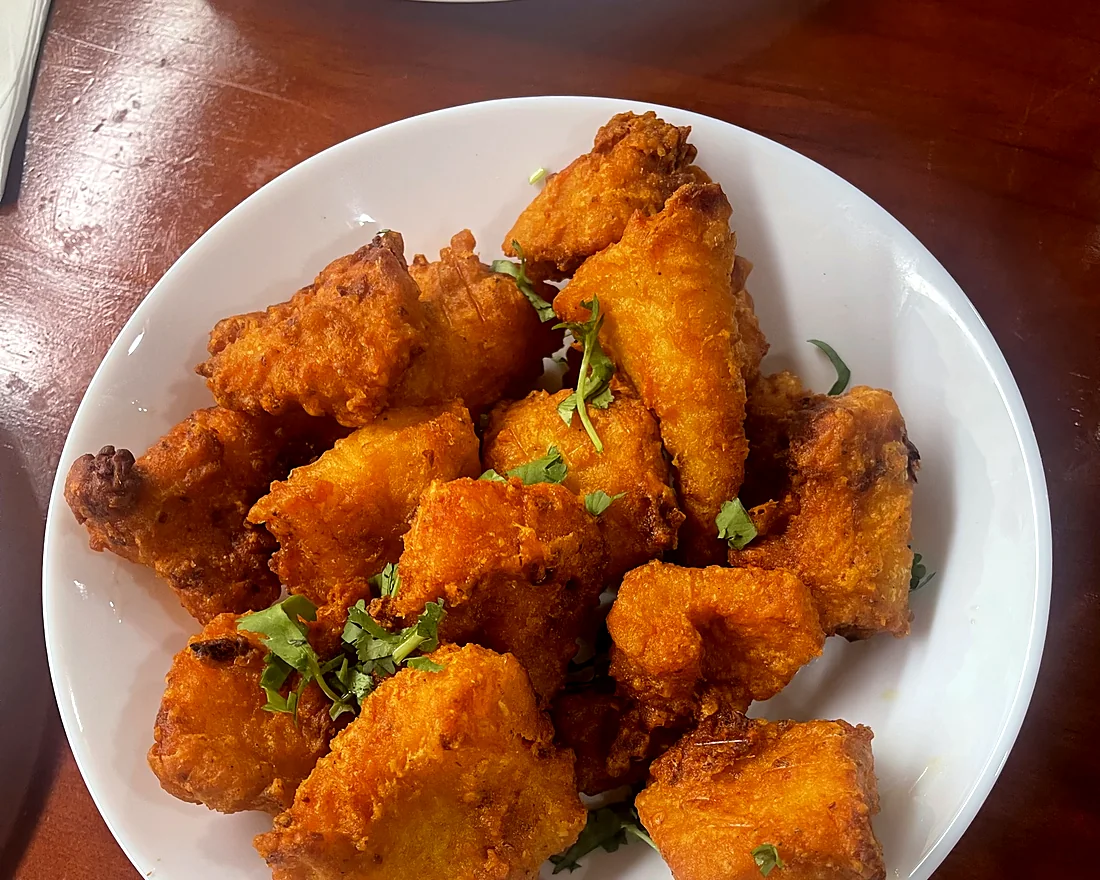 Plate of crispy orange-battered fried fish pieces sprinkled with coriander