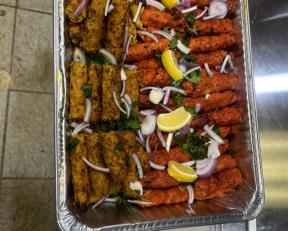 Catering tray of seekh kababs and chicken tikka with lemon wedges and onions
